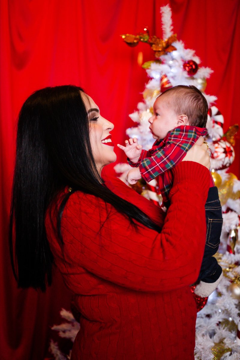 Una mamá levantando a su bebé y sonriéndole, con el árbol blanco detrás