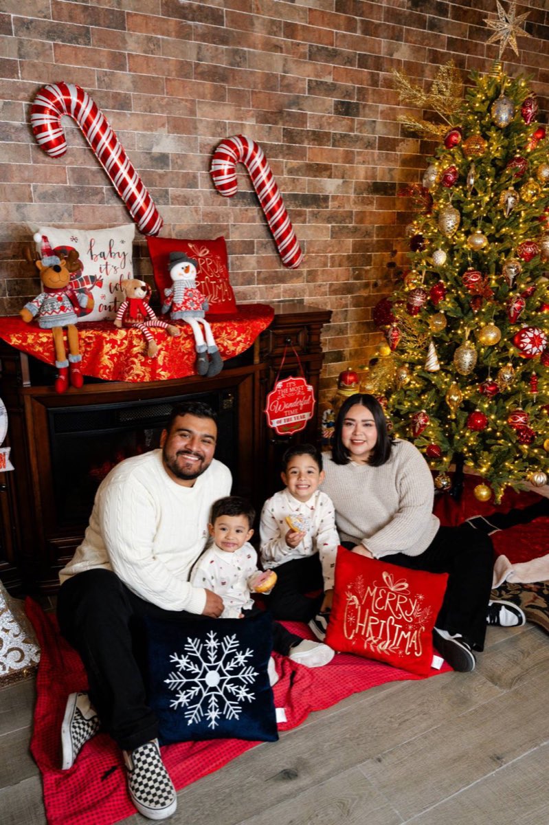 Familia de cuatro sentada frente a la chimenea y el árbol del set navideño