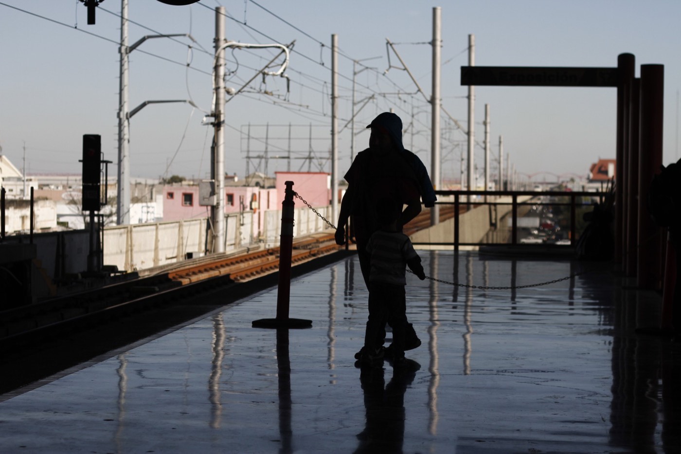 Siluetas de un papá con su niño en el andén del metro de Monterrey, a contraluz, con las vías y los postes detrás.